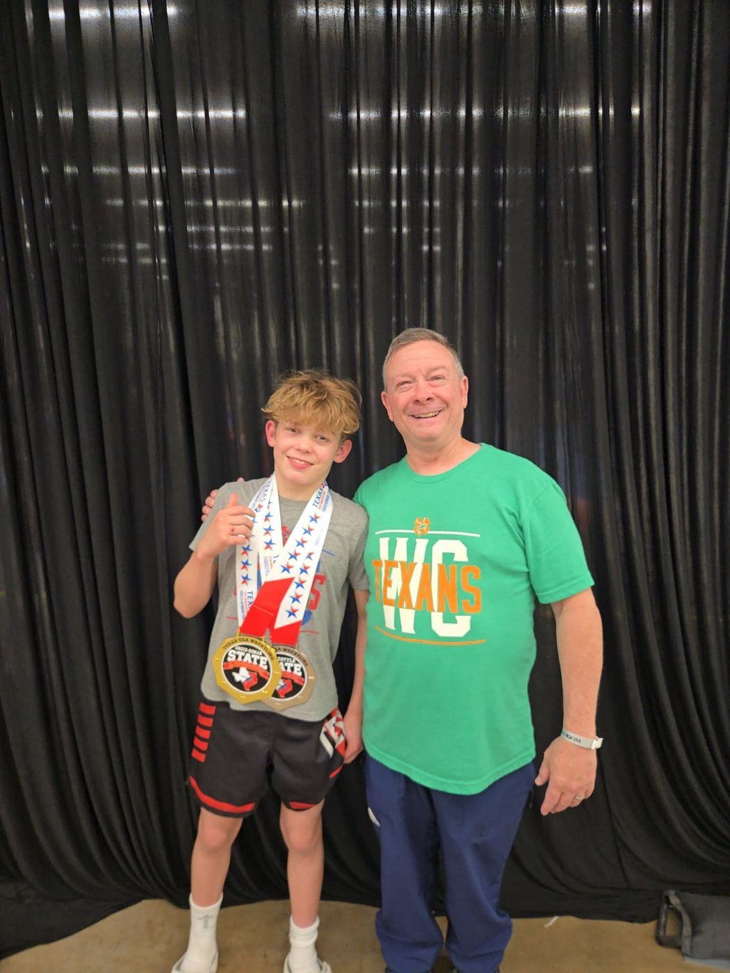 Lucas wearing his Greco-Roman state gold medal and freestyle state silver medal, next to Coach Nick McClellan